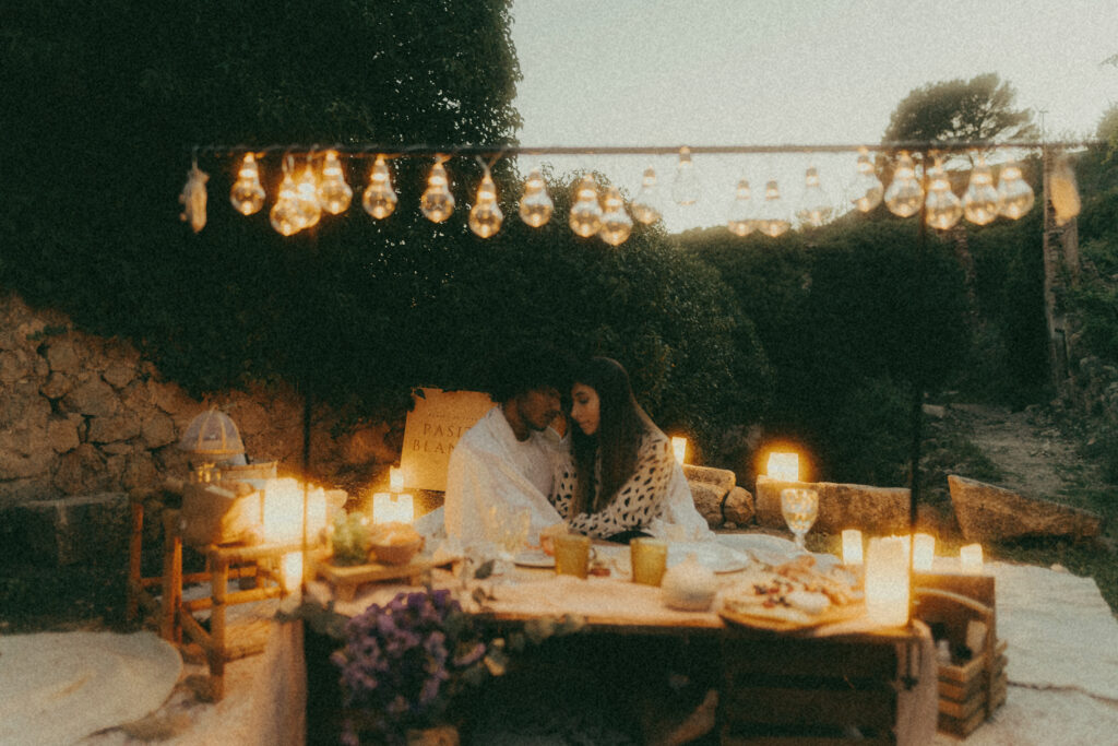 Pareja disfrutando de un picnic decorado elegantemente con luces en el atardecer